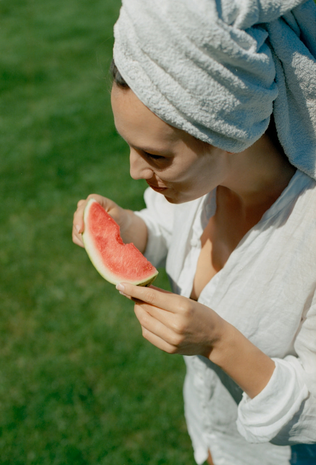 A woman with a towel on her head eating a watermelon
